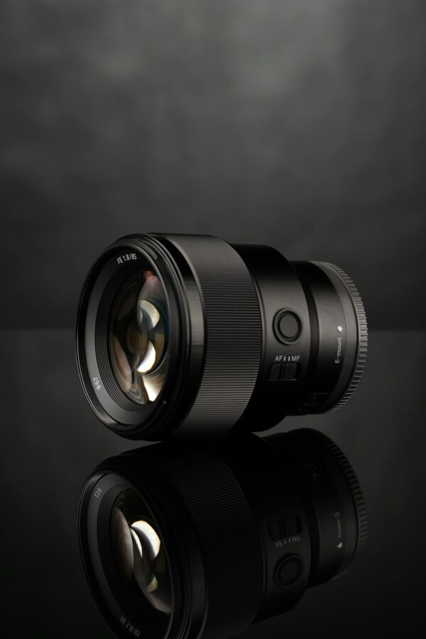 Close-up of a professional camera lens on a reflective black surface, ideal for technology and photography themes.